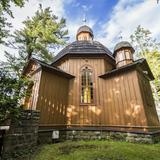 Niewielki drewniany kościółek przypominający swoją architekturą małą cerkiew. Stoi pośród drzew.