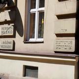 Fragment elewacji budynki z dwoma oknami i napisami w języku polskim i jidysz: Herbata, mleko i różne przekąski.