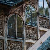 Trzy drewniane okna z łukiem, dzielone na pół, umieszczone w jaskółce pod dachem pokrytym gontem. Nad oknami i pod nimi drewniane zdobienia z sercem pośrodku.