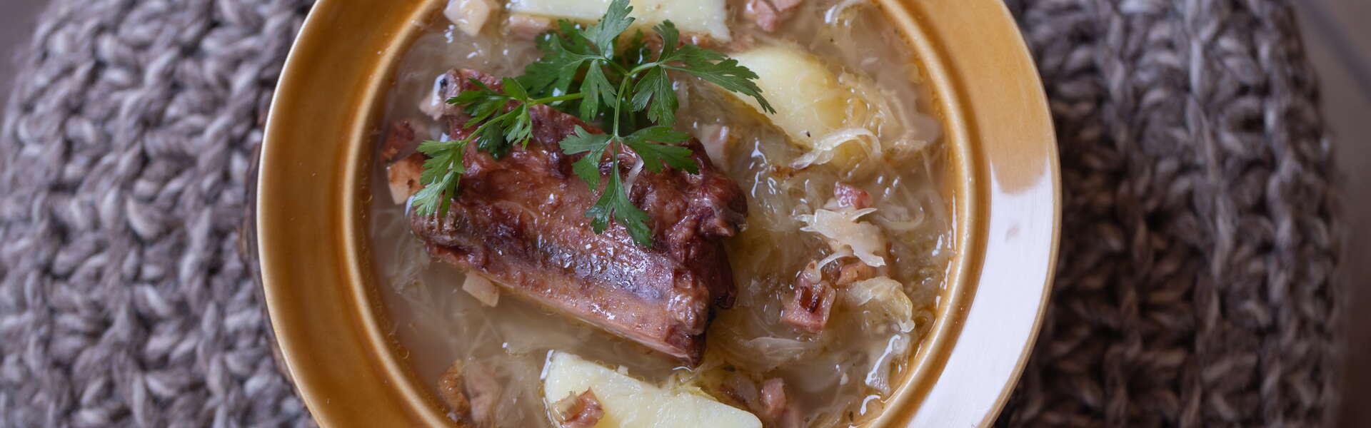 Talerz z zupą z kapusty kiszonej - kwaśnicą, z kawałkiem żeberka, ziemniakami i skwarkami, widziany z góry.