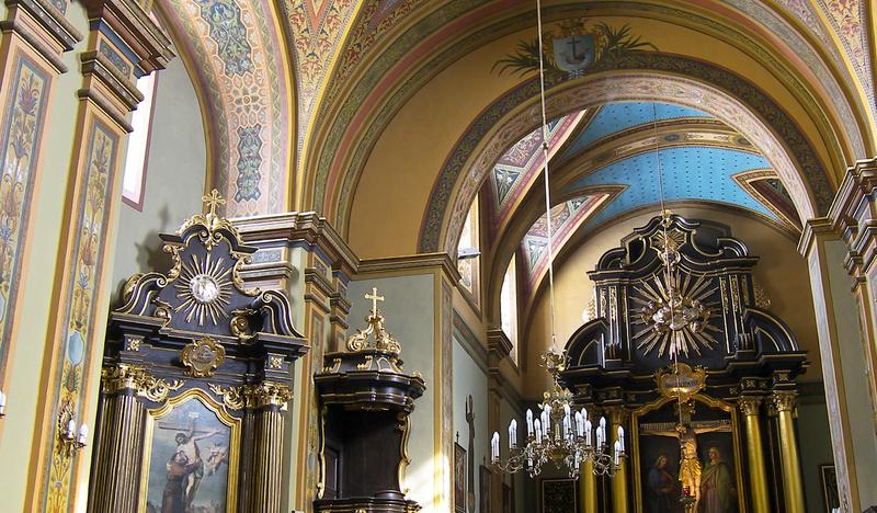 Wnętrze kościoła. Ołtarz główny z rzeźbą Chrystusa Ukrzyżowanego, ołtarz boczny i ambona w ciemnym kolorze. W nawie drewniane ławki.