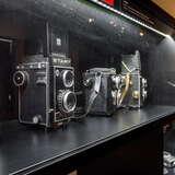 Urządzenia fotograficzne na ciemnych półkach w szklanej gablocie w Muzeum Fotografii w Krakowie.
